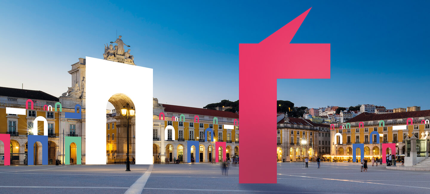 Praça iluminada ao entardecer com arco central, luzes coloridas e escultura vermelha moderna.